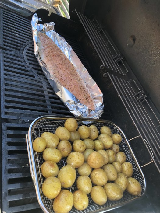Laxfilé kryddad på folie och grillade småpotatisar på en grill.