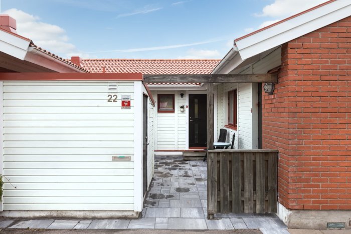 Entré till ett 80-tals radhus med vit garageport, tegelmur och ventilation i grunden.