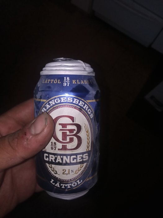 Hand håller krossad ölburk av märket Ångesbergs före duschen, med skadat finger.