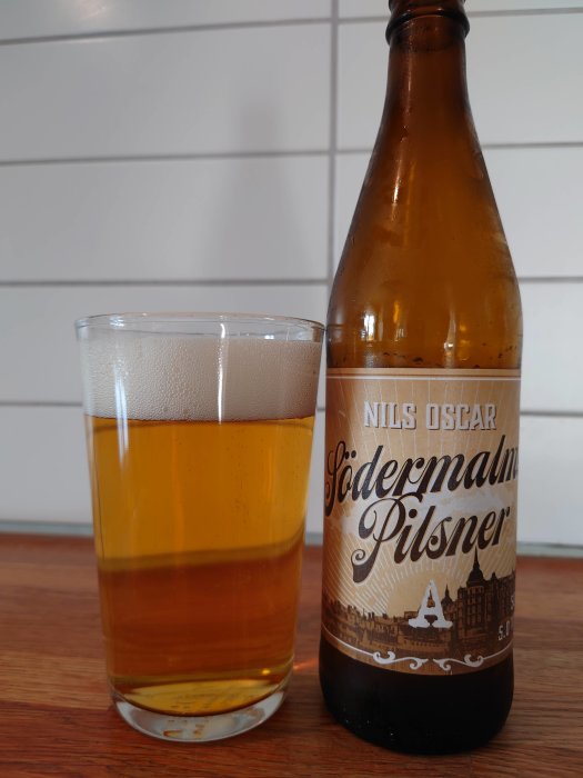 En ölflaska av Södermalms Pilsner bredvid ett glas med öl på en träyta.