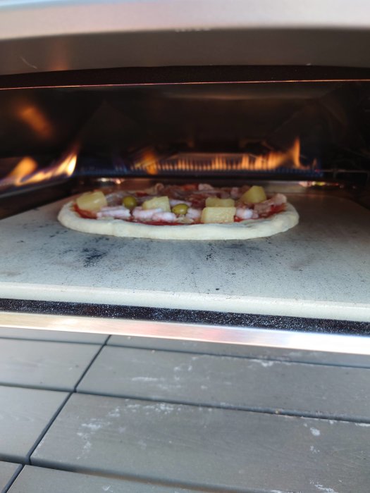 En pizza med skinka och ananas gräddas i en vedeldad ugn.