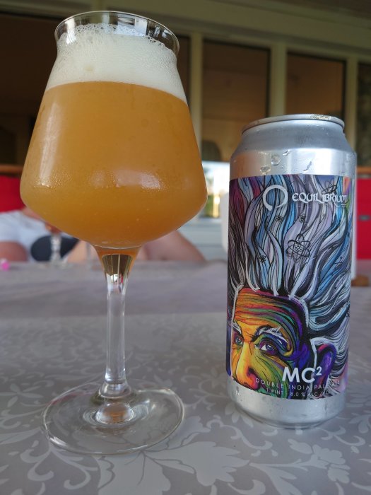 Ett glas med skummande öl bredvid en konstnärligt designad ölburk på ett bord.