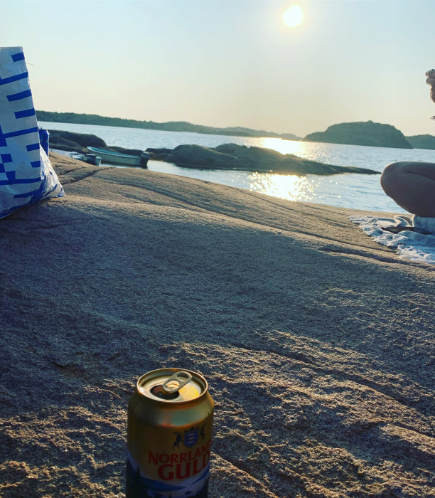 Ölburk på stranden vid solnedgång, strandväska och del av person i förgrunden.