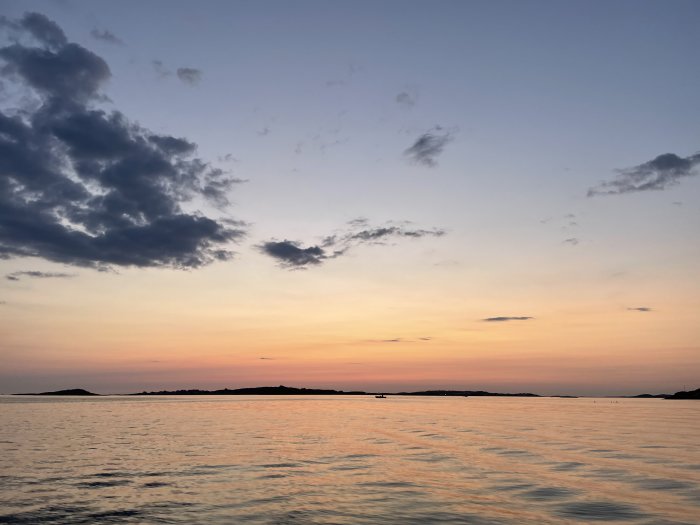 Solnedgång över havet med moln och silhuetter av öar i bakgrunden.