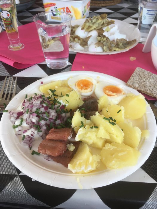 Tallrik med matjessill, färskpotatis, hackad rödlök, halverat ägg och knäckebröd, traditionell svensk måltid.