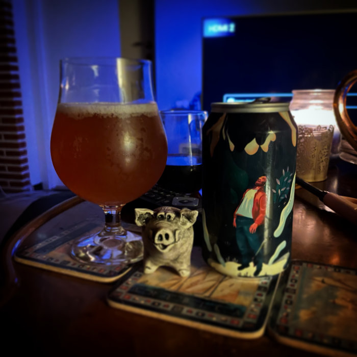 Ölglas fyllt med öl och konstnärligt designad ölburk på ett bord framför en datorskärm.