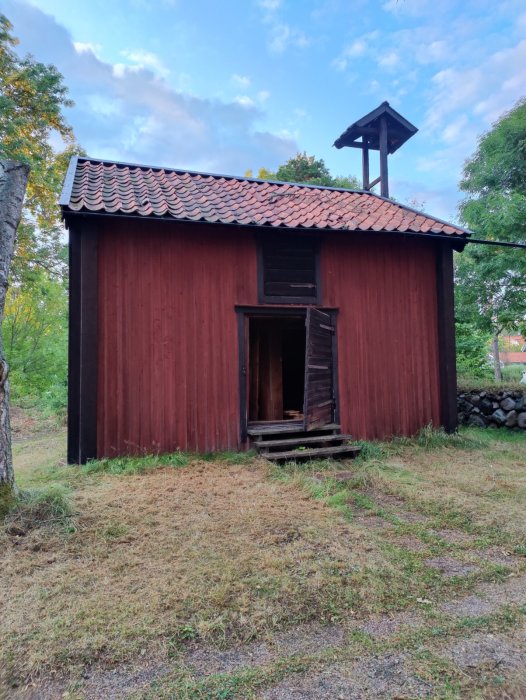 Gammalt rött hölager med öppen dörr och skadat tak som omvandlingsprojekt till bostadsyta.