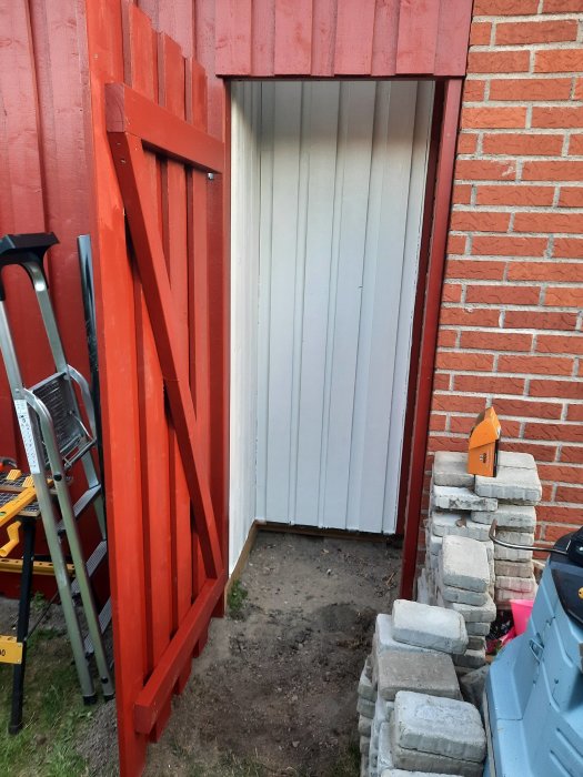 Nyinstallerad vit dörr med rött dörrkarm på ett tegelhus, omgiven av byggmaterial.