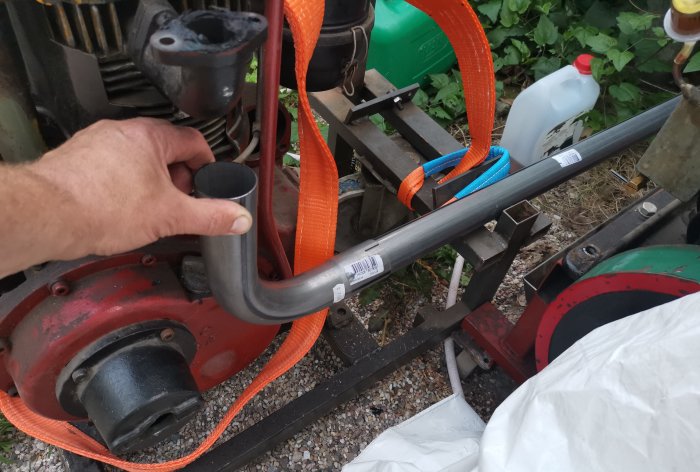 Hand som håller i ett böjt metallrör nära en motor med orange sjöräddningsremmar i bakgrunden.