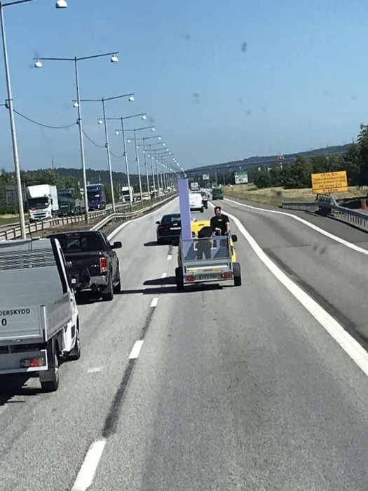 Trafik på E4:an med en bil som drar ett släp med företagslogga under en solig dag.