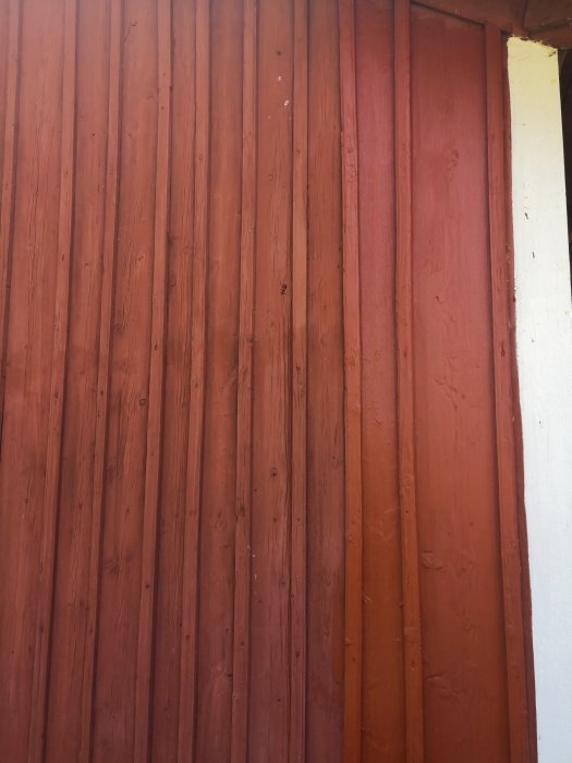 Rödmålade träpaneler på en vägg med varierande brädbredd, vissa för smala för en roller.
