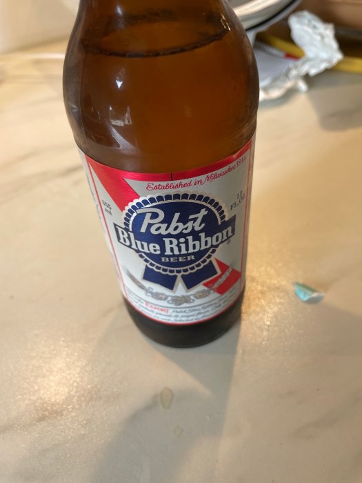 Flaska med Pabst Blue Ribbon öl på ett bord, delvis drucken med bakgrundsoskärpa.