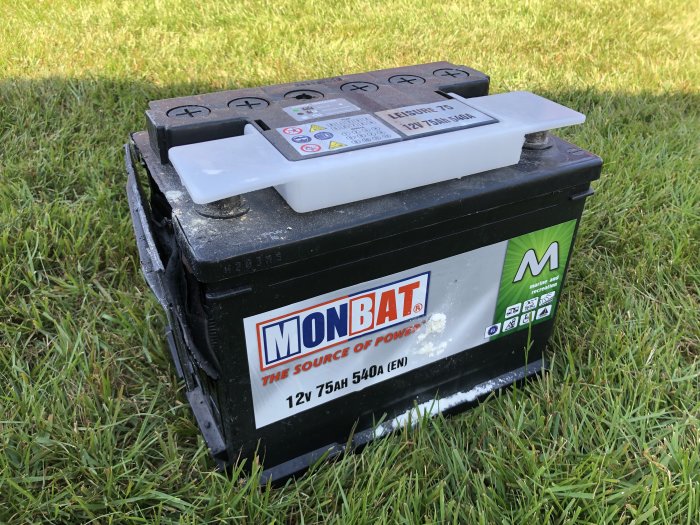 Bilbatteri av märket MONBAT på gräs, använd för husvagnens 12-volts system.