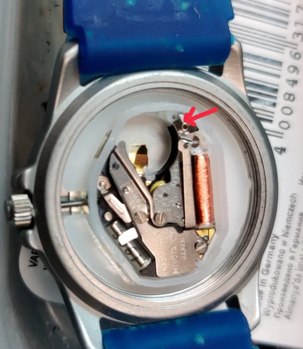 Armbandsurets inre med öppen batterifack och synlig mekanism, skruv markerad med röd pil.