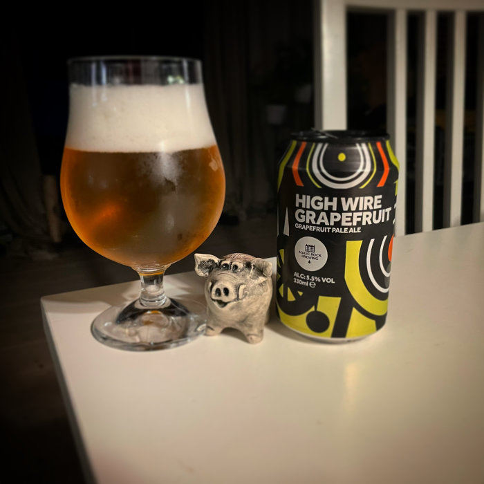 Ölglas med skummad öl bredvid en burk High Wire Grapefruit Pale Ale och en liten grisknäckesburk.