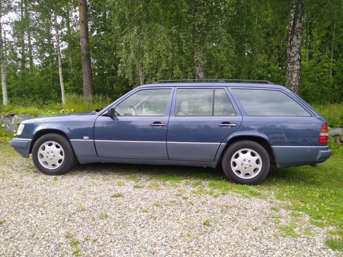 Nauticblå Mercedes E280 kombi från sidan med beige interiör och landskapsbakgrund.