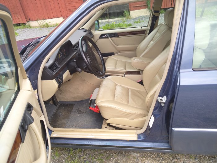 Interiör av en nauticblå Mercedes E280 med beige skinninredning och öppen förardörr.