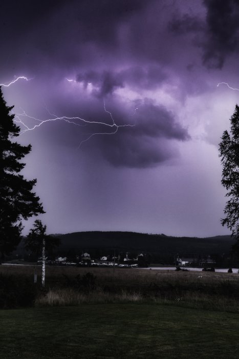 Åskväder över landskap med blixtrar i lila himmel ovanför ett småhusområde.