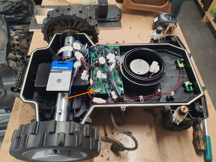Robotklippare öppnad för batteribyte, inuti syns elektronik och komponenter samt nytt CR1225 batteri.