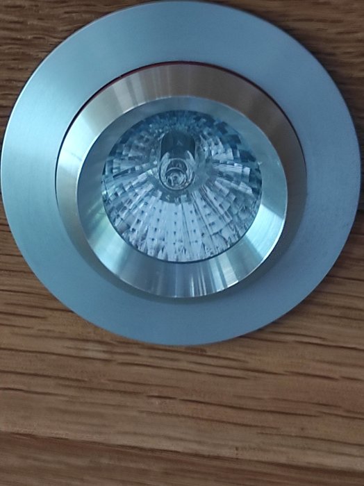 Närbild av en inbäddad takspotlight med synlig glödlampa mot träbakgrund.