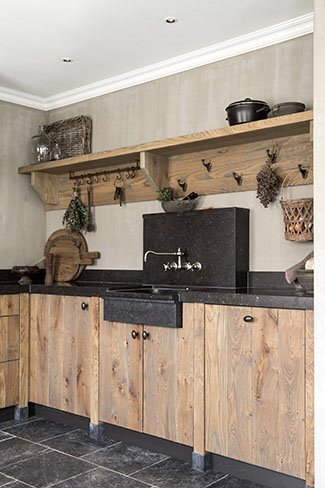 Rustikt kök med träskåp, svart bänkskiva och öppna trähyllor med dekorativa föremål.