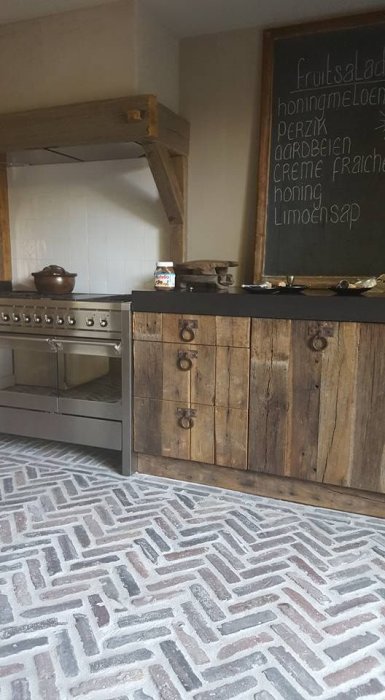 Rustikt kök med träskåp, stenugn och svart bänkskiva, kritskrivtavla med text på väggen.