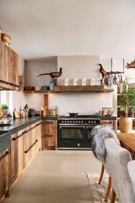 Rustikt kök med träskåp, stenbänkar och modern spis, med prydnadsfåglar på hylla.