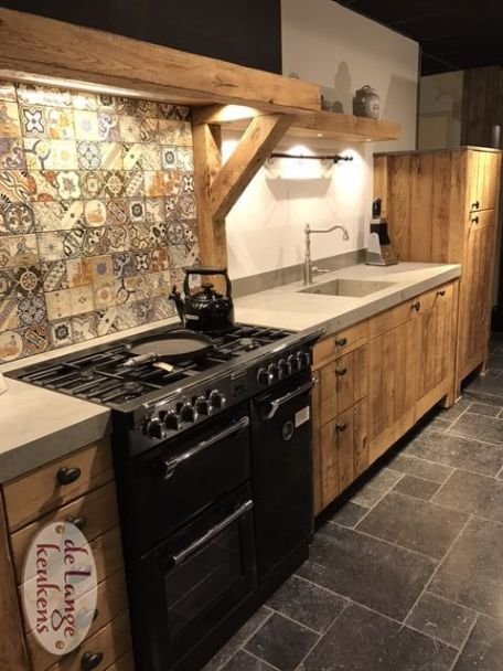 Lantligt kök med träskåp, mönstrade kakel och svart spis.