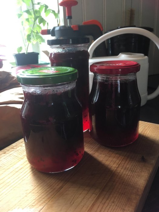 Två glasburkar med hemgjord mörkröd marmelad på ett träbord.