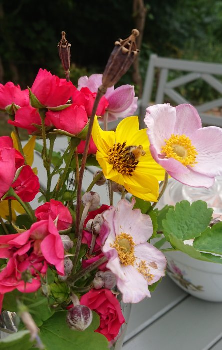 En humla pollinerar en präriesolros omgiven av rosor och andra blommor i en bukett utomhus.