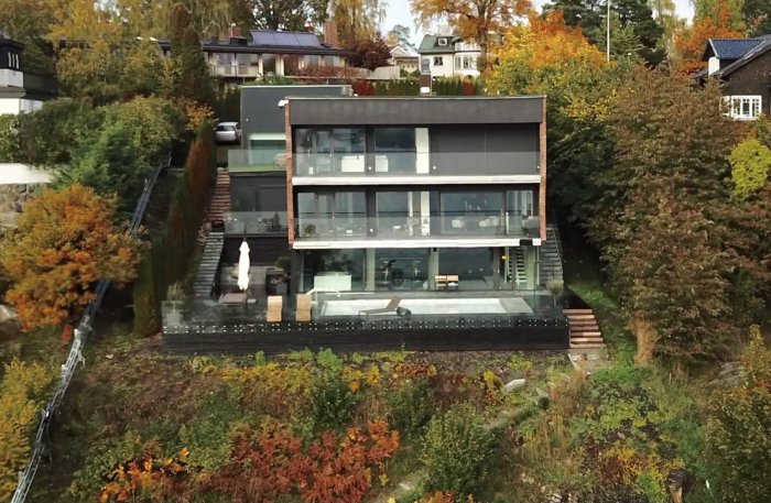 En modern villa på Lidingö med stora fönster, terrasser och omgiven av höstfärgad vegetation.