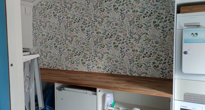 Nyuppsatt blommig tapet och träbänkskiva i ett kök under renovering.