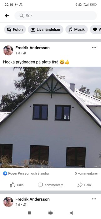 Vit husfasad med svart tak och nyinstallerad dekorativ nock på gaveln.