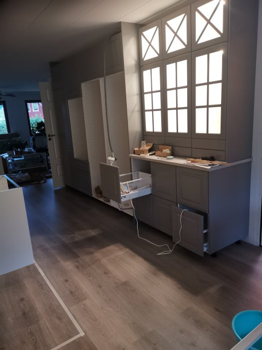 Kök under renovering med öppna skåp och ett litet hål i väggen nära taket för elinstallation.