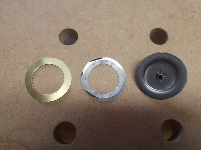 Mässingsplåt shims och täcklock på arbetsbänk för montering, illustrerar byggprojektets delar.