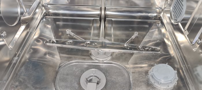Interiör av en öppen diskmaskin som visar korgarrangemang och spolarmar.