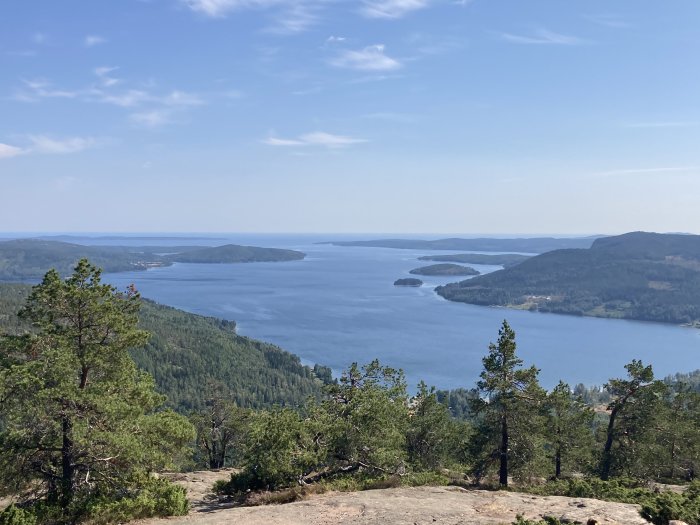 Utsikt från ett berg över en skog och en sjö med öar under en klarblå himmel.