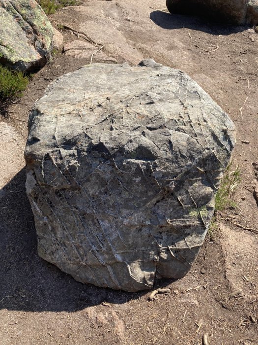 Stor stenblock med tydliga sprickor i naturlig miljö på marken.