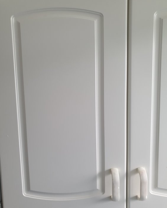 Ett par vita badrumsskåpsdörrar med slitna plasthandtag från 90-talet, avstånd på ca 65 mm mellan hålen.