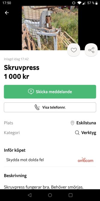 Gammal skruvpress i metall på ett arbetsbänk utomhus.