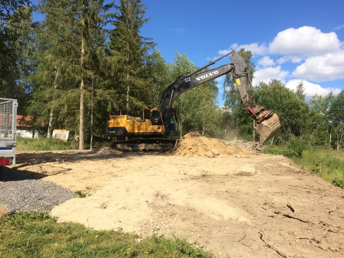 Grävmaskin arbetar med att jämna ut mark och röja träd på en byggtomt.