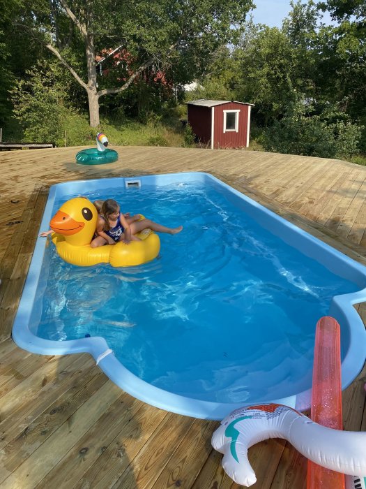 Nybyggd trädäck runt en ovanmarkspool med uppblåsbara leksaker och barn som leker.