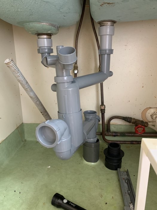 Vattenlås och rörinstallation under en handfat med synliga rörstammar och ej monterad gumminippel.
