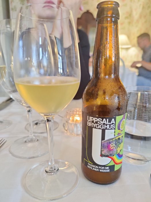 Öppnad flaska veteöl från Uppsala Brygghus bredvid ett glas med öl på ett bordsduk.