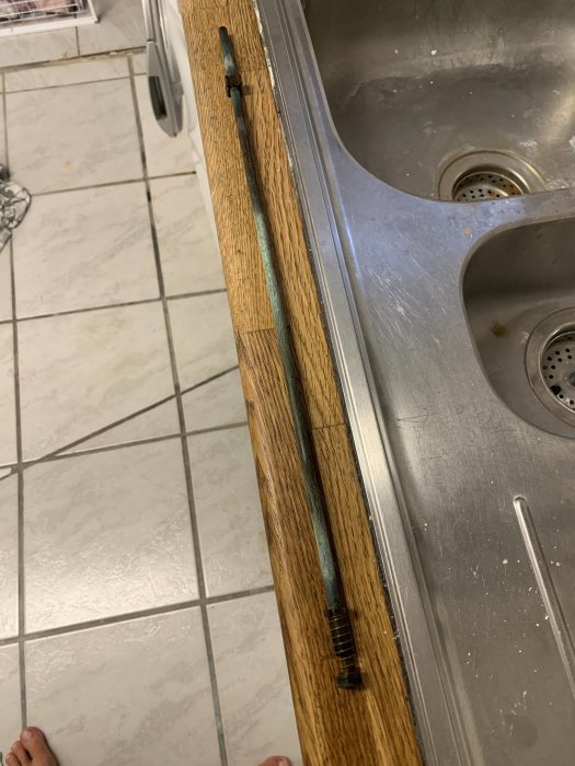 Delar av en vattenutkastare bredvid ett handfat på en träbänk som behöver reparation.