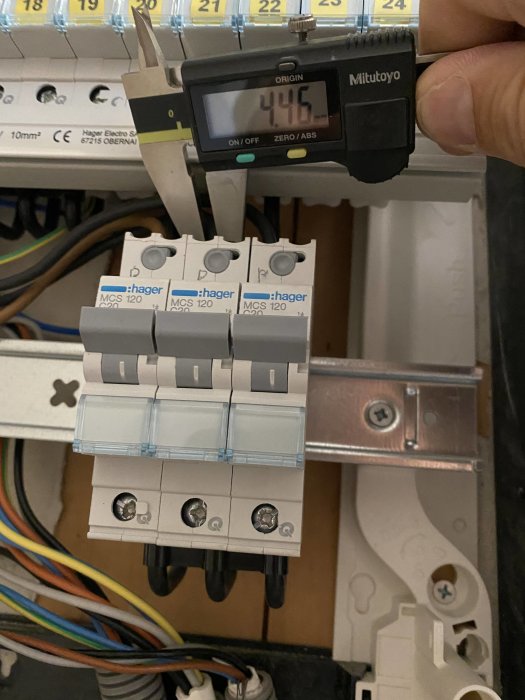 Ett skjutmått mäter diameter på en elektrisk kabel framför tre säkringar i ett elektriskt skåp.