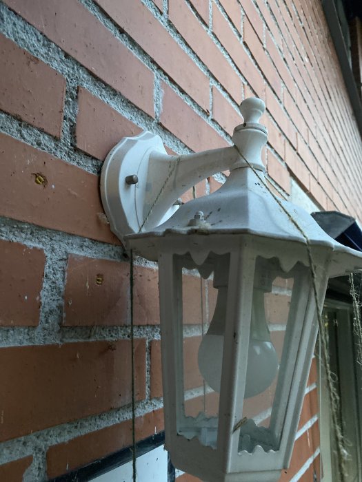 Gammal utomhusvägglampa monterad på en tegelvägg vid en husentré, potentiell källa för eldragning.
