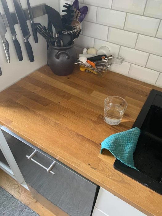 Köksbänk i trä med klibbig yta, omgiven av knivar, köksredskap och en blå trasa.