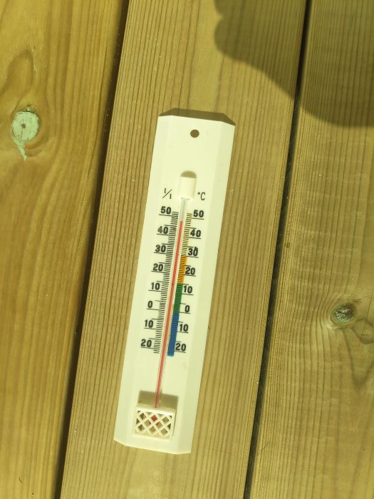 Trädäck med monterad analog termometer som visar temperatur runt 25 grader Celsius.