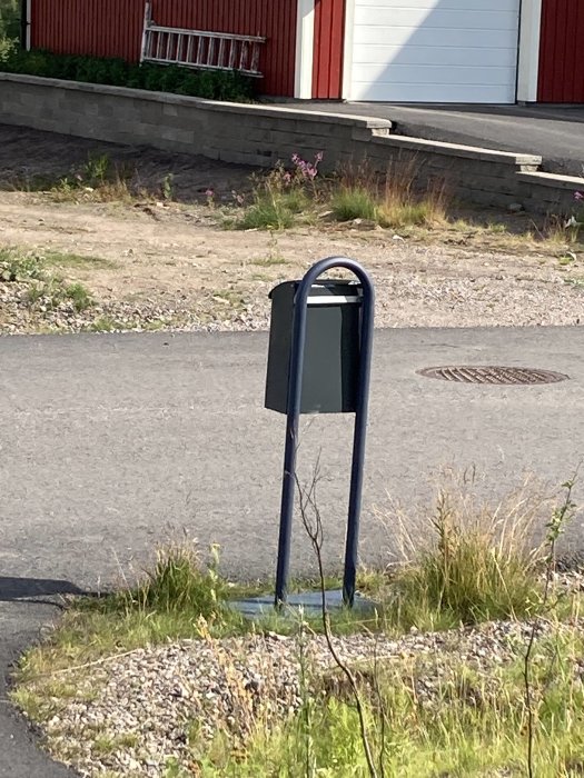 Ett nykonstruerat brevlådestativ av metall på en grusgång med ett hus i bakgrunden.